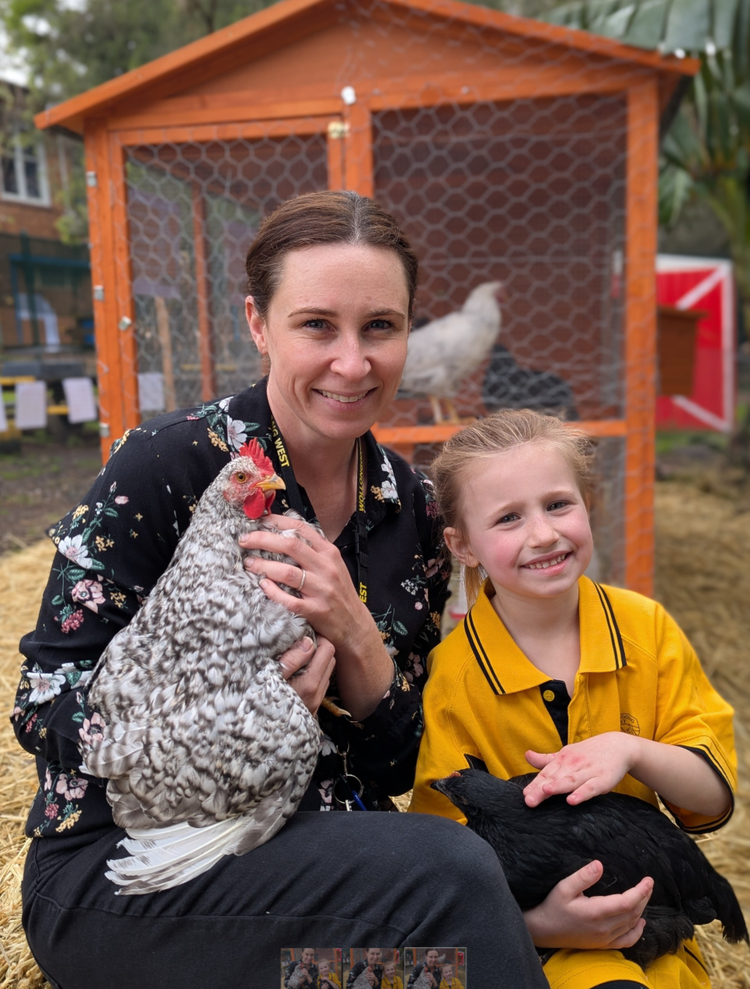 Teacher and a student holding chickens in front of a coop.